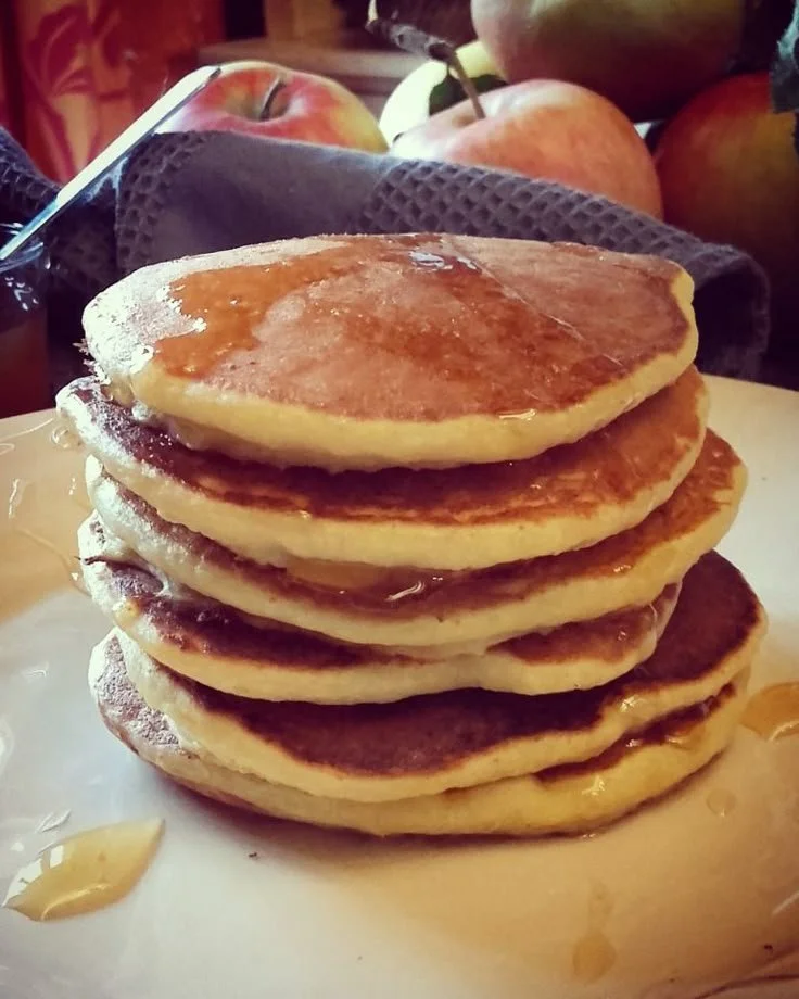 Pancakes à la compote de pomme dorés sur une assiette, garnis de morceaux de pomme.